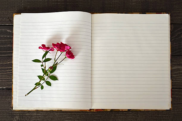 Åpent notatblokk på et trebord med en penn og noen tørkede blomster ved siden
